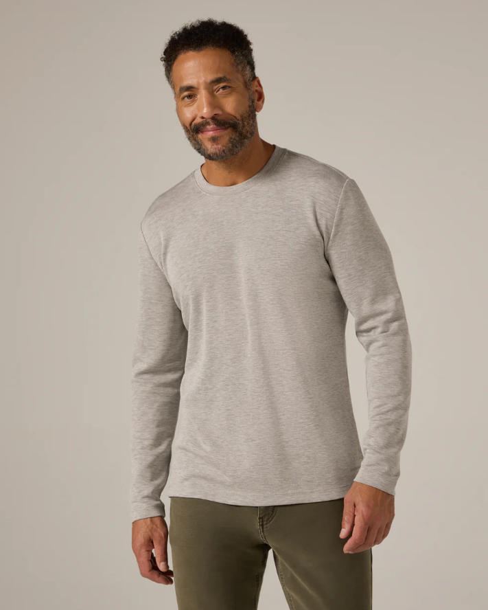 Man wearing a gray long-sleeve shirt and green pants against a plain background