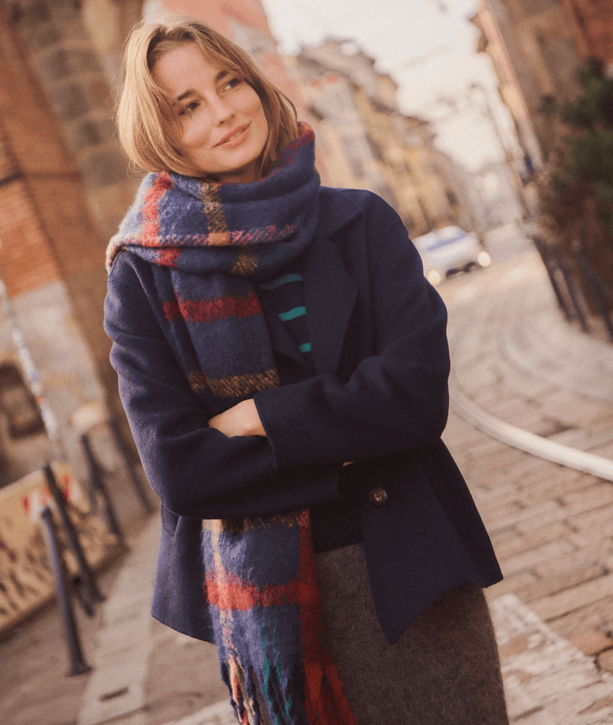 Woman wearing a dark coat and colorful scarf on a street.