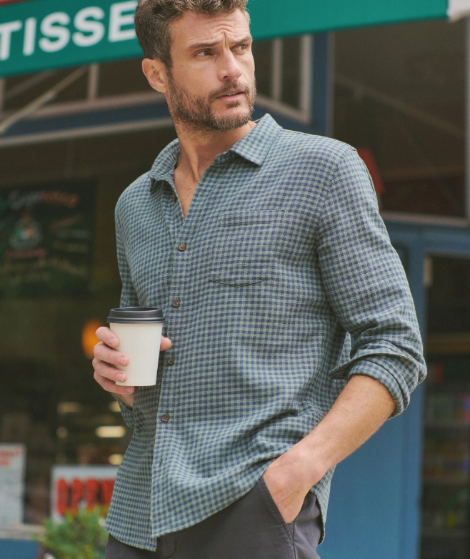 Man in a blue and green checkered shirt holding a coffee cup outdoors