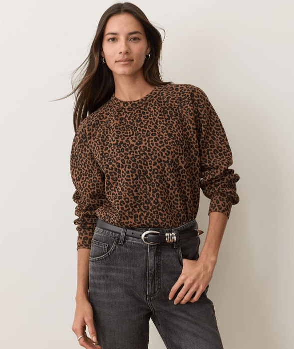 A woman wearing a leopard print sweartshirt and black jeans on a white background