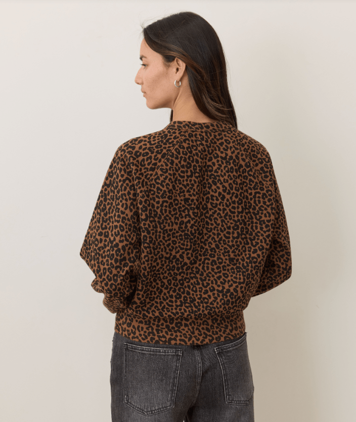 Rear view of a woman wearing a leopard print sweartshirt and black jeans on a white background