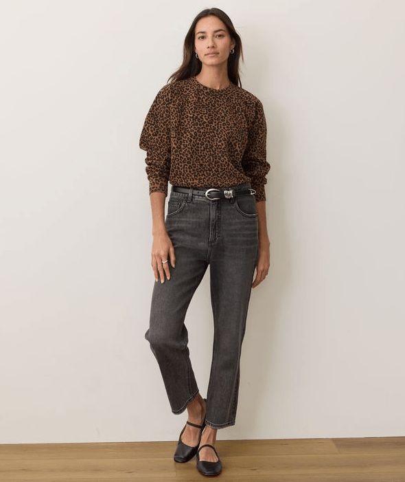 A woman wearing a leopard print sweartshirt and black jeans on a white background