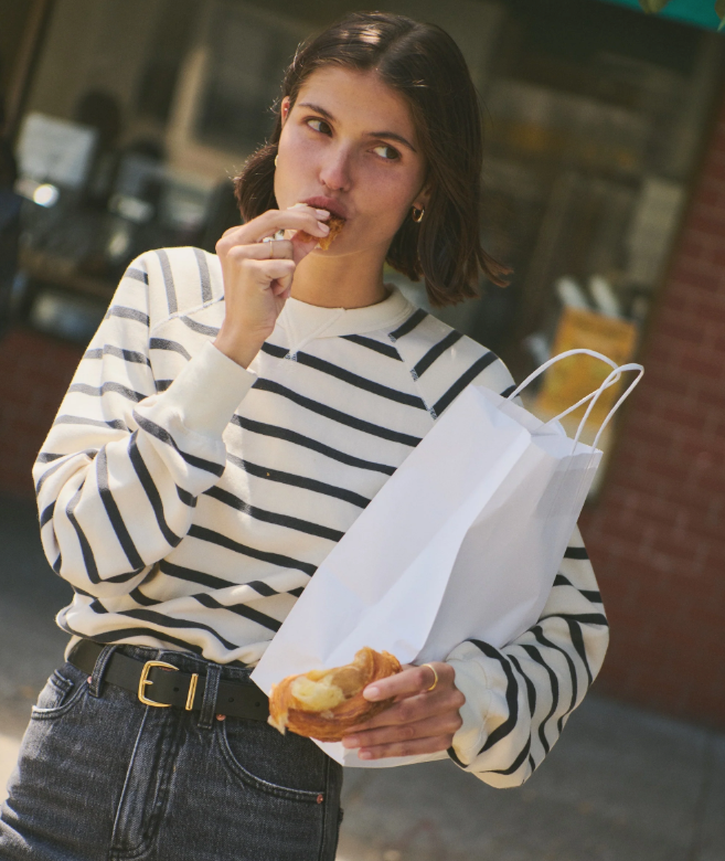 Woman in a black and white striped sweater eating outdoors with a paper bag.
