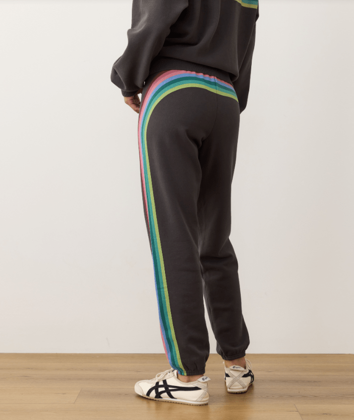 Black sweatpants with colorful stripes on a wooden floor and white wall background