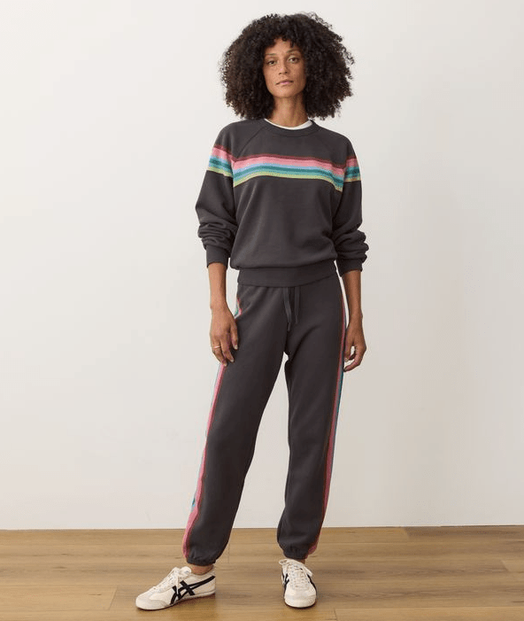 Person wearing a black sweatsuit with colorful stripes on a white background