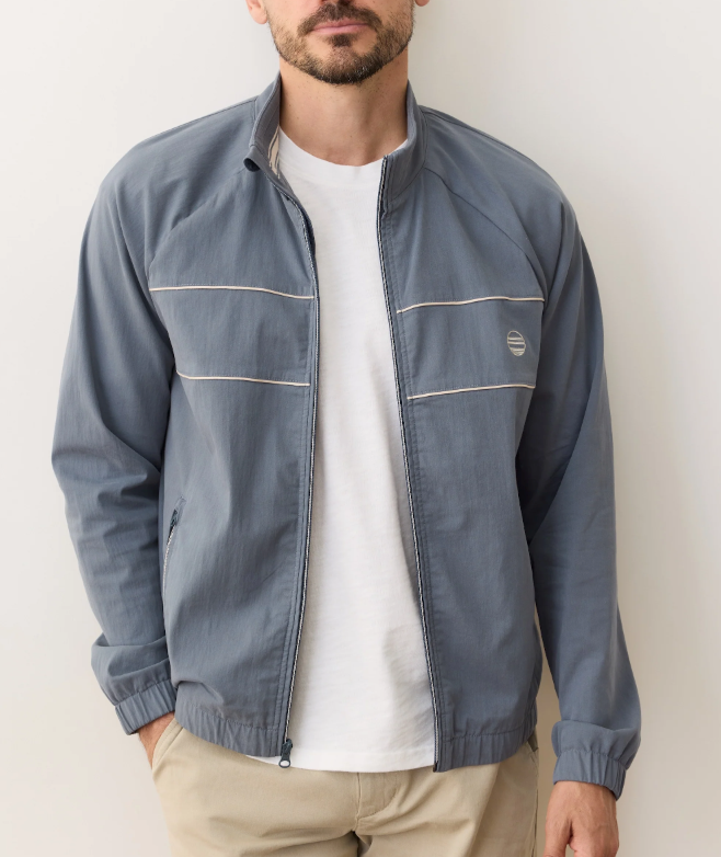 Man wearing a blue windbreaker over a white shirt with a visible brand logo on a plain background