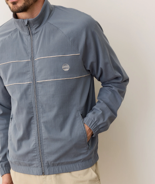 Man wearing a blue windbreaker with a logo on a plain background