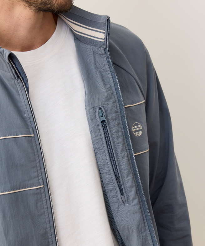 Close-up of a person wearing a blue windbreaker with a brand logo on a neutral background
