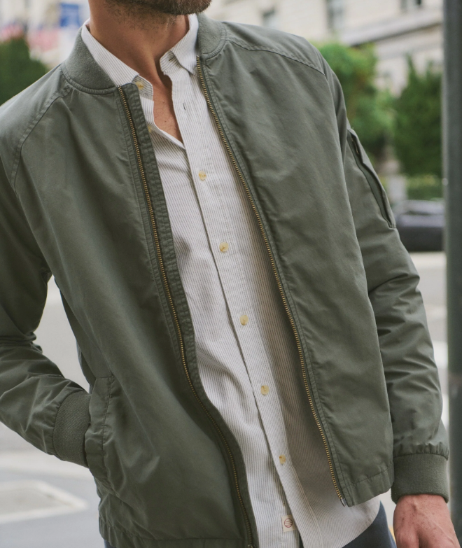 Person wearing a green bomber jacket over a white shirt with a blurred background
