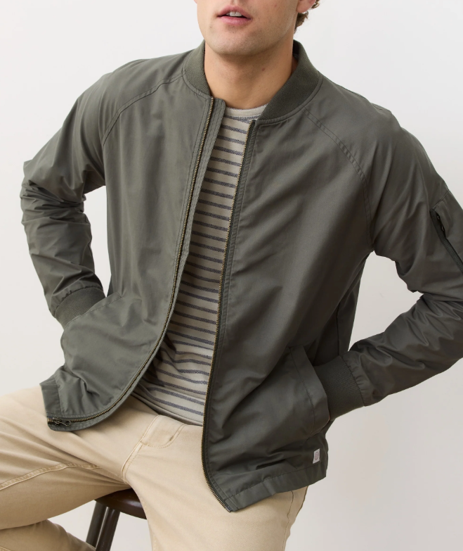 Man wearing a green bomber jacket over a striped shirt with a neutral background