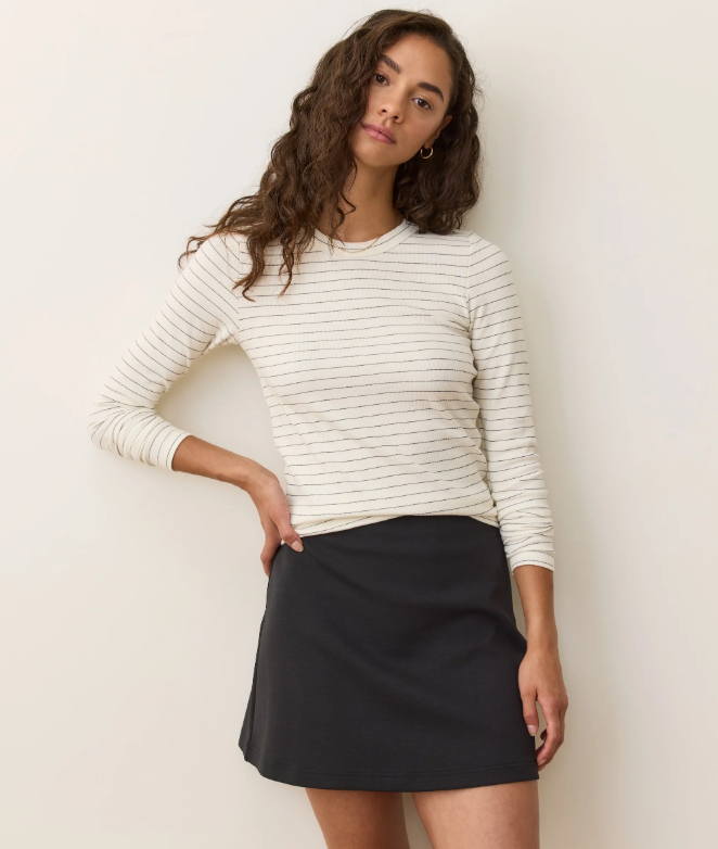 Woman wearing a white longsleeve shirt with black stripes and black skirt against a plain background
