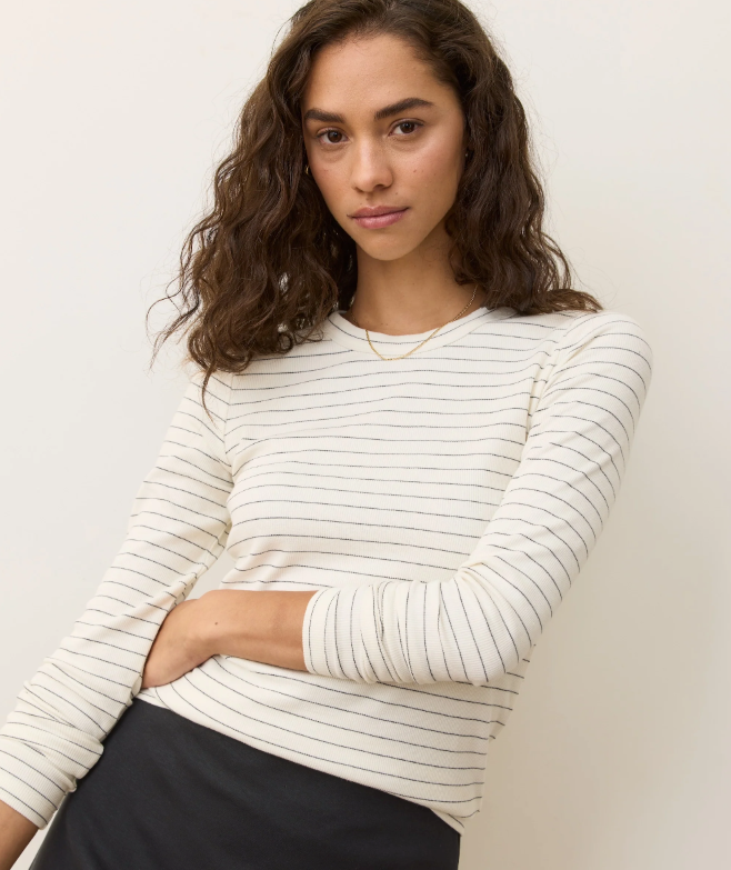 Woman wearing a white longsleeve shirt with black stripes against a plain background