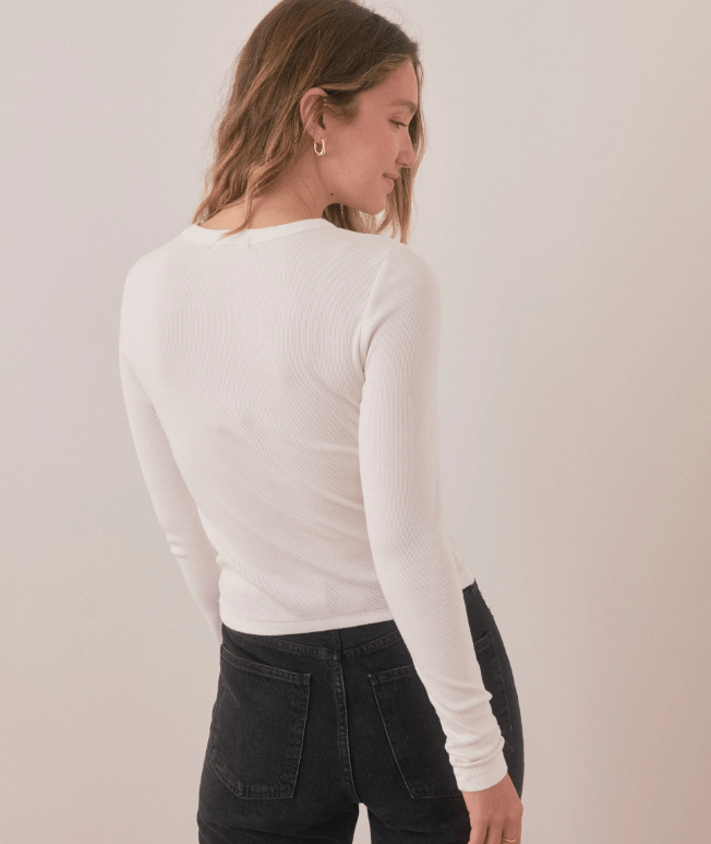 Woman wearing a white long-sleeve top and black pants against a plain background