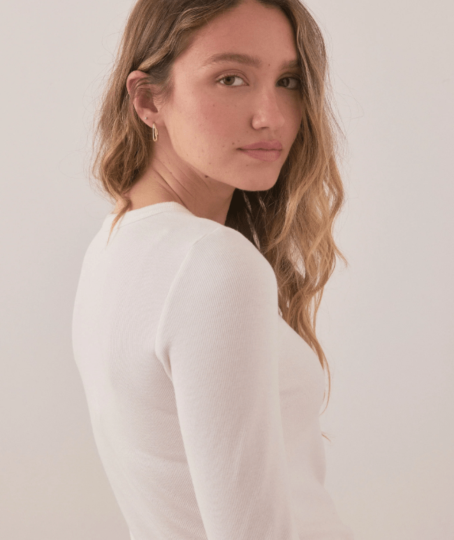 Woman wearing a white long-sleeve shirt against a plain background