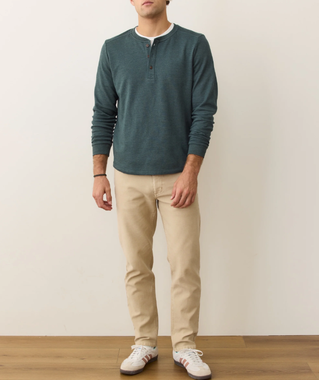 Man wearing a green long-sleeve henley and beige pants against a plain background
