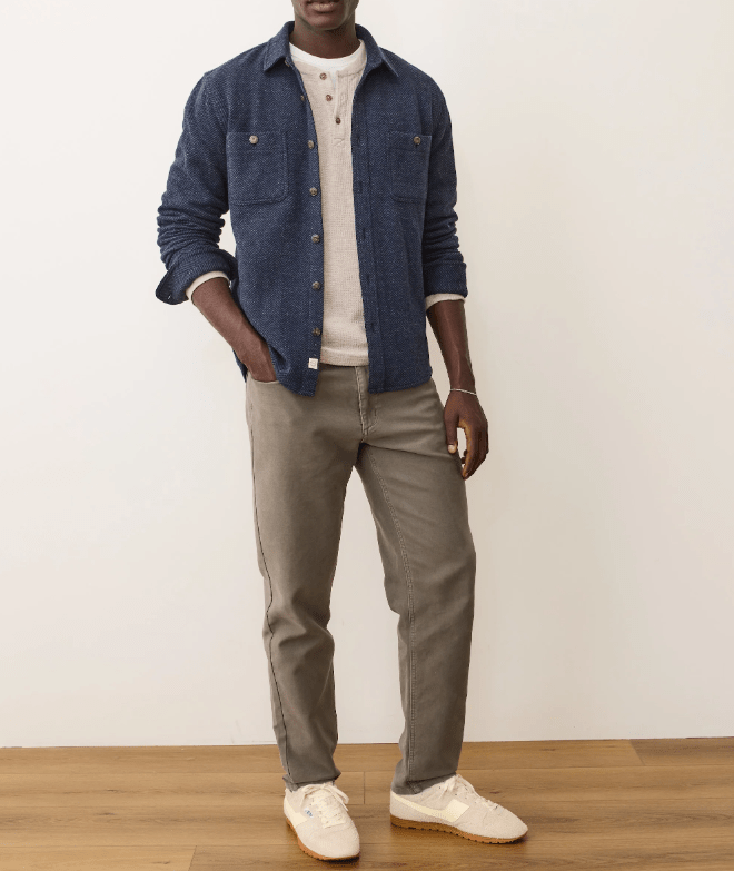 Man wearing a blue overshirt, white henley, gray pants, and white sneakers on a plain background