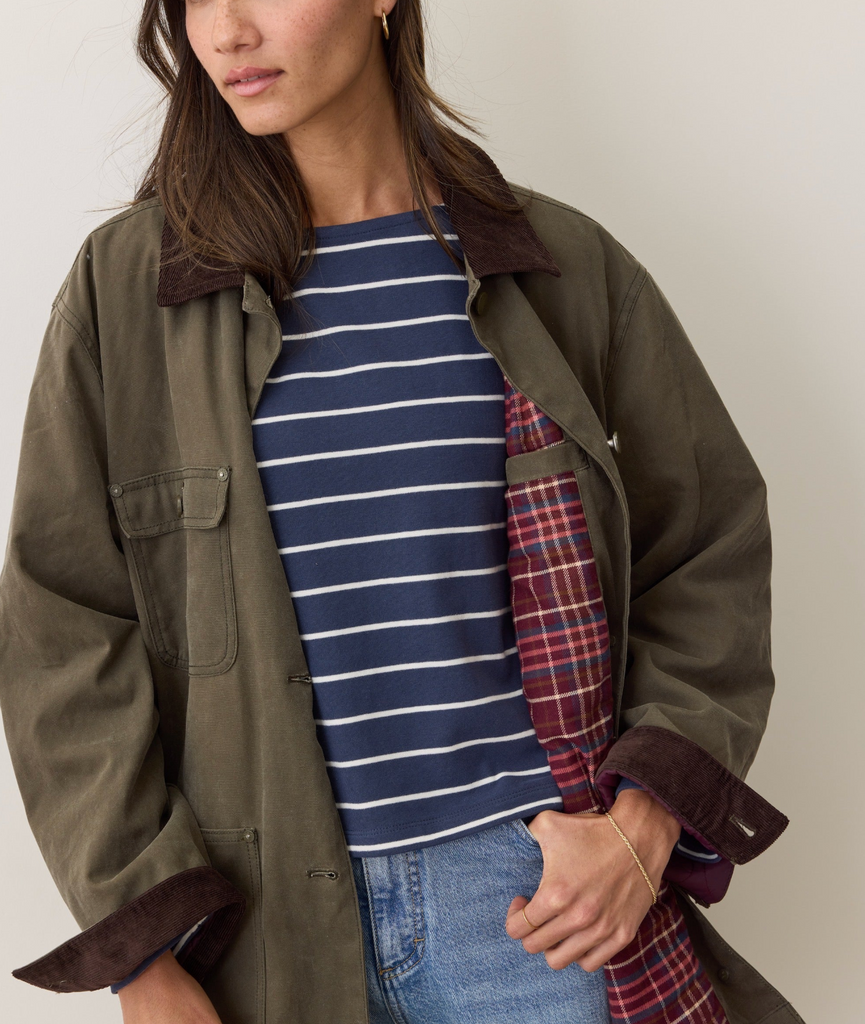 Woman wearing a green jacket with a plaid lining over a striped shirt on a plain background