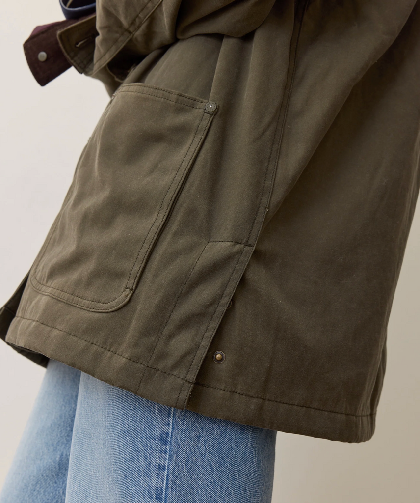 Close-up of a woman wearing a green jacket with a pocket and button on a neutral background