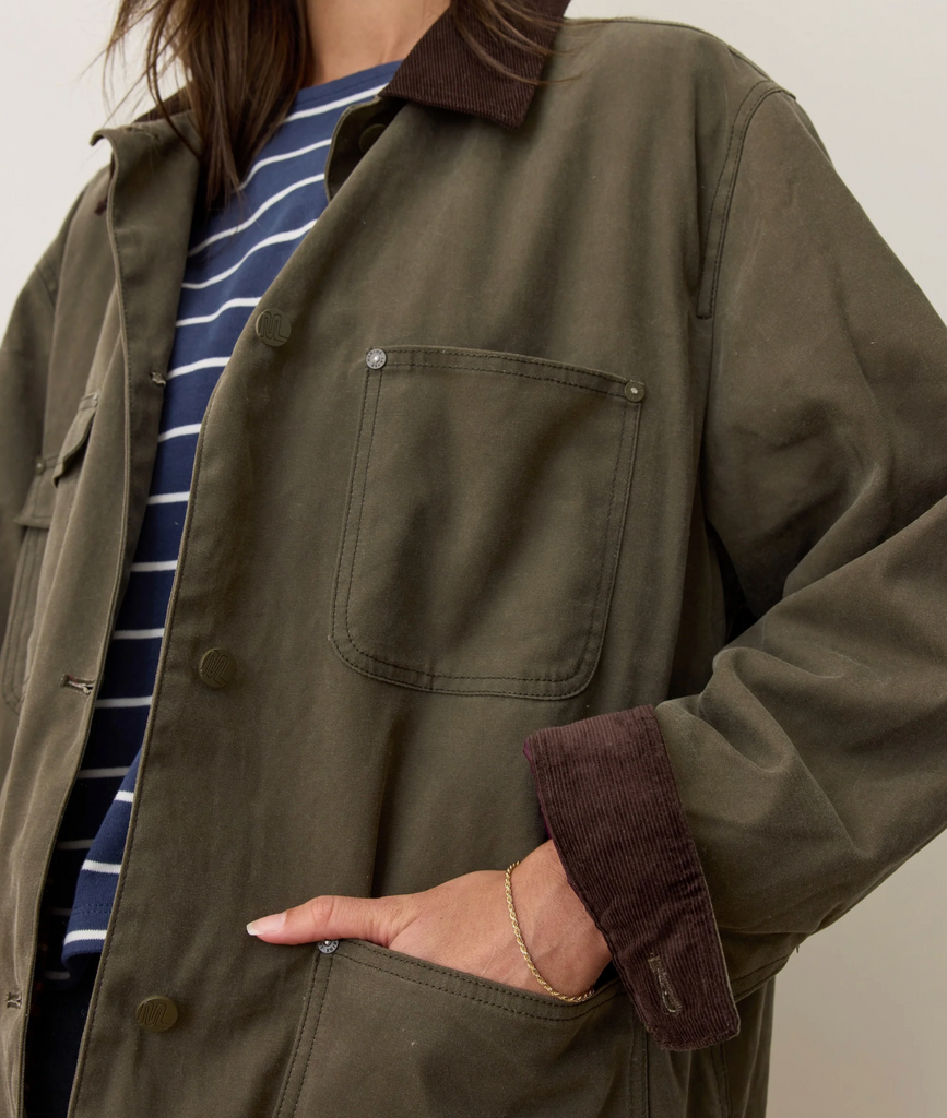 Woman wearing a green jacket with a striped shirt underneath on a neutral background