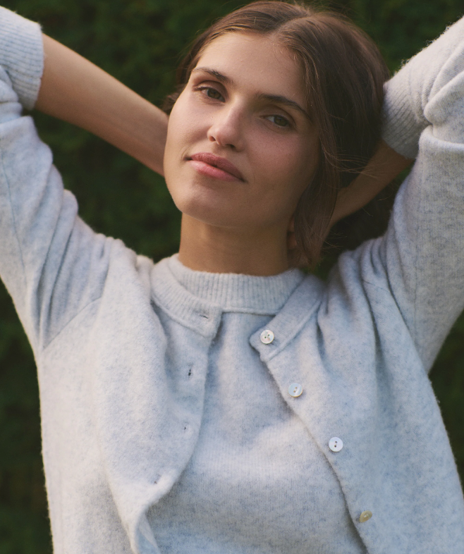 Woman wearing a light blue cardigan with a blurred green background