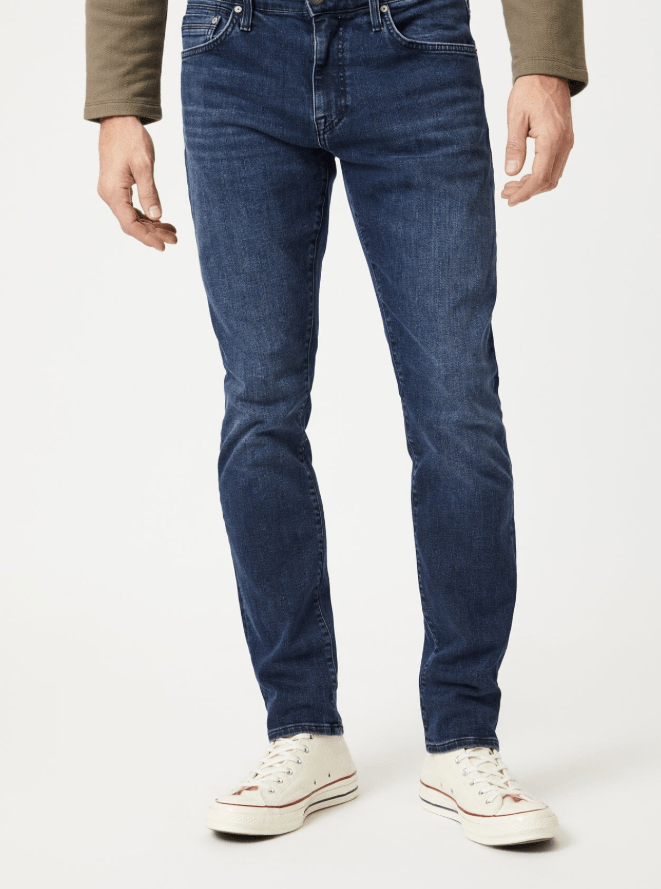 Man wearing blue jeans and white sneakers on a plain background