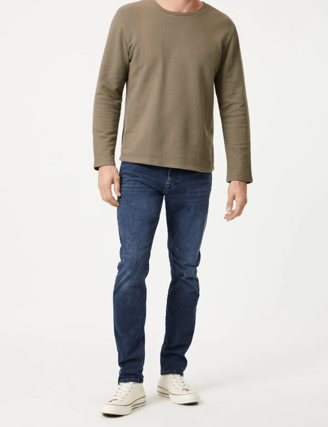 Man wearing a green long-sleeve shirt and blue jeans on a white background