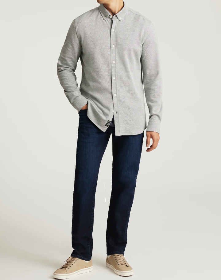 Man wearing a gray button-up shirt and dark jeans on a white background