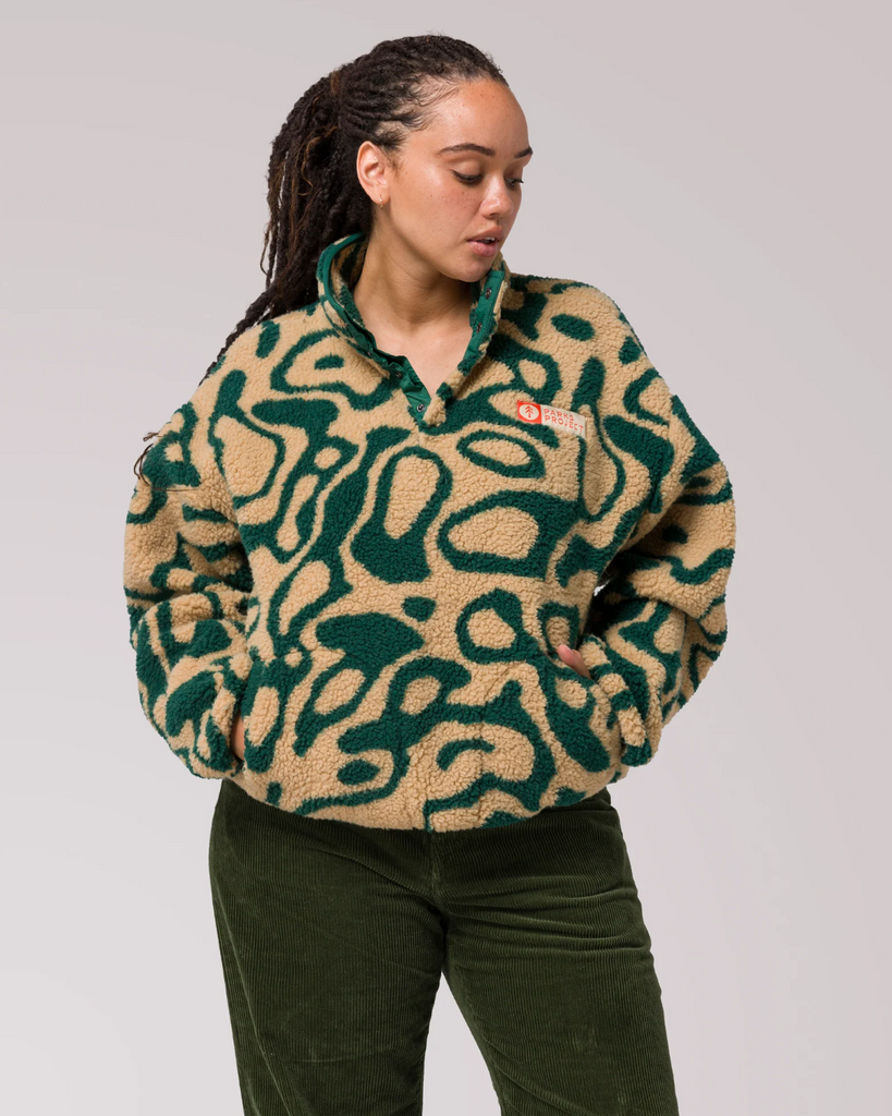 A woman wearing a green and yellow patterned sweater on a plain background