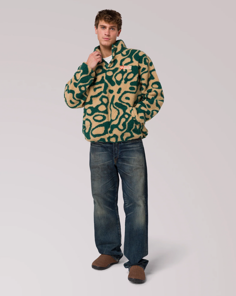 Man wearing a yellow and green patterned fleece jacket with jeans on a plain background