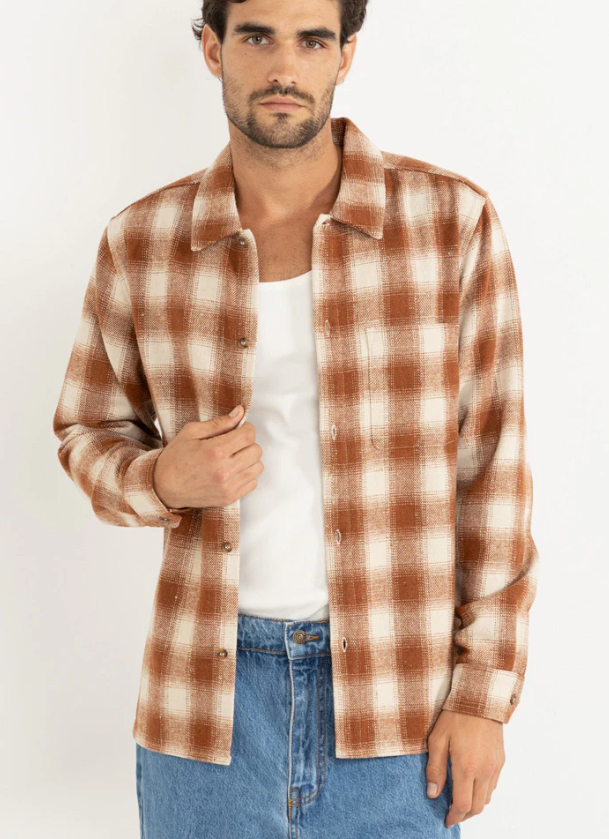 Man wearing a burnt orange and white checkered shirt over a white t-shirt with blue jeans on a white background