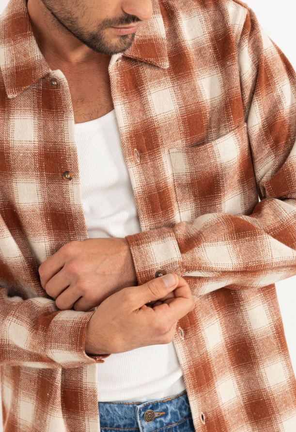 Man wearing a burnt orange and white checkered shirt over a white t-shirt.
