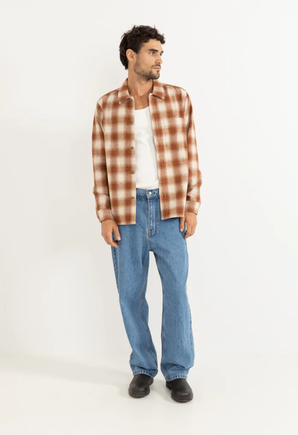 Man wearing a burnt orange and white plaid shirt and jeans on a white background