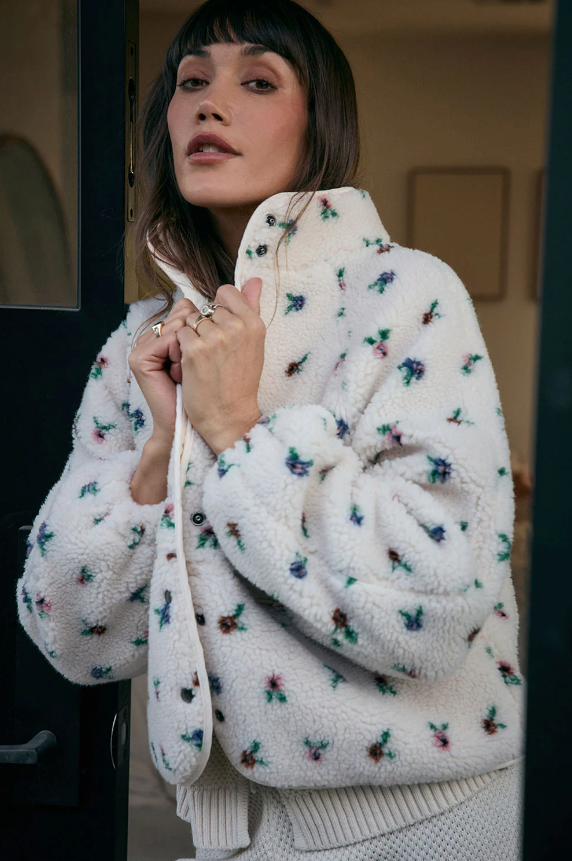 Woman wearing a white floral-patterned fluffy bomber coat with a blurred background