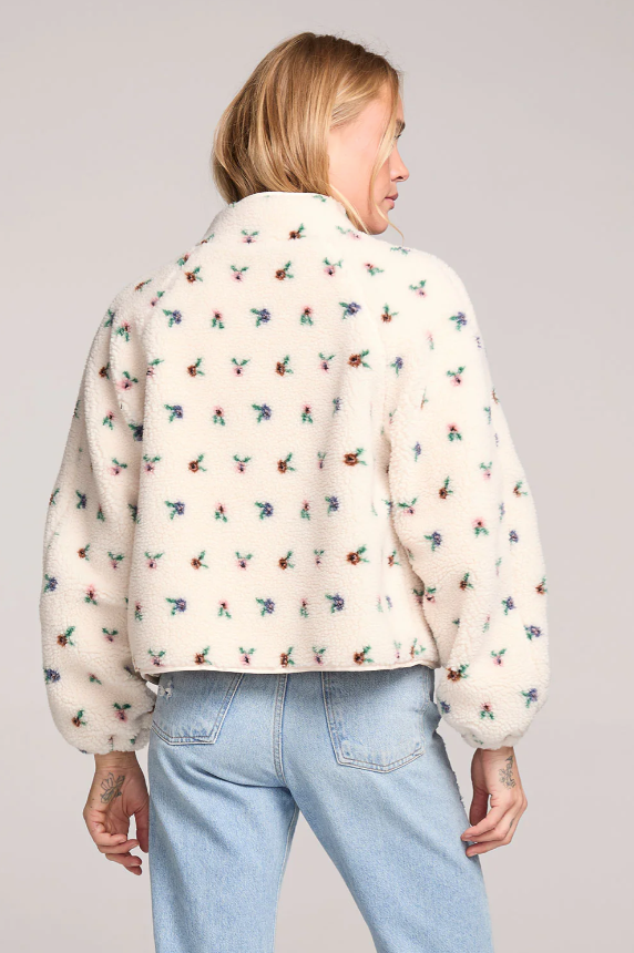 Person wearing a cream-colored fluffy jacket with colorful floral patterns on a plain background