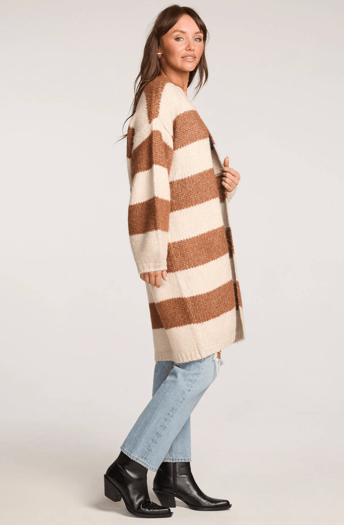 Woman wearing a long brown and cream striped cardigan and light blue jeans on a white back ground