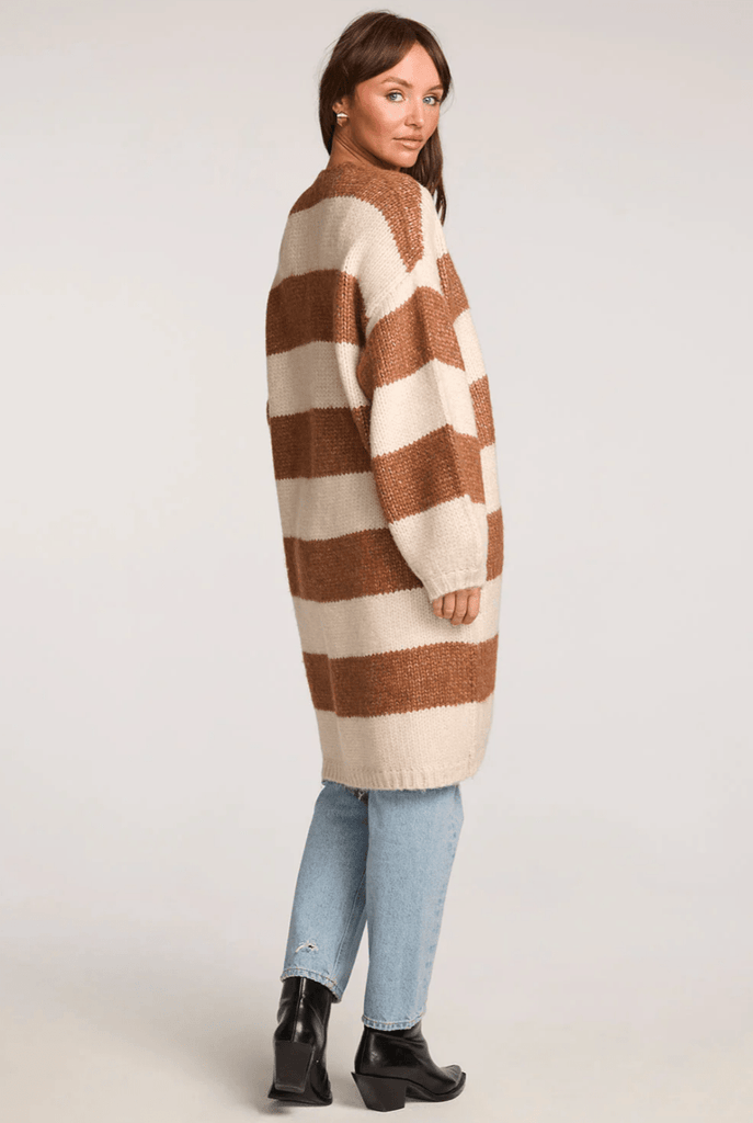 Woman wearing a long brown and cream striped cardigan and light blue jeans on a white back ground