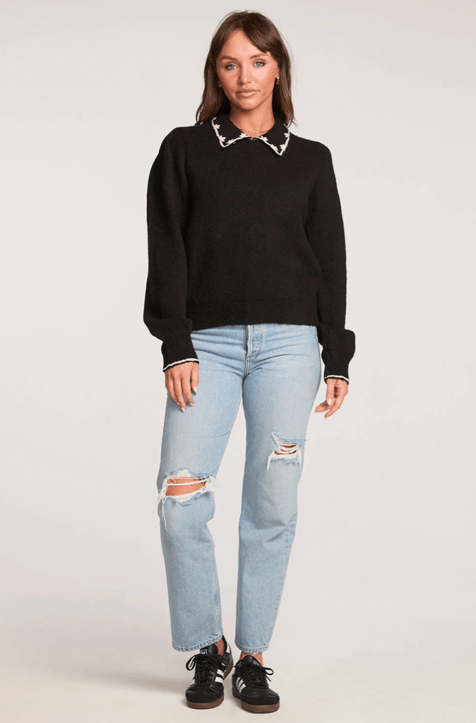 Woman wearing a black sweater and light blue jeans on a white background