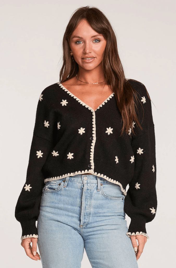 Woman wearing a black cardigan with a white floral design on a white background