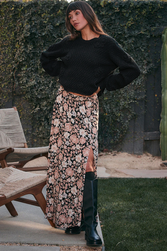 Woman wearing a black sweater and floral midi skirt with a slit standing outdoors.