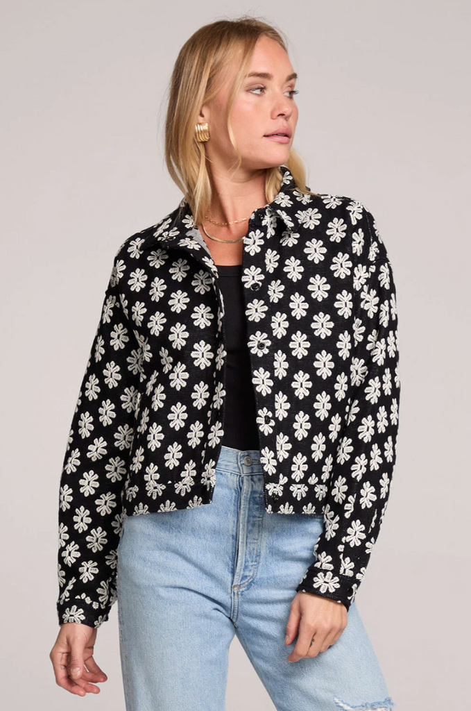 Woman wearing a black floral jacket with light blue jeans on a plain background