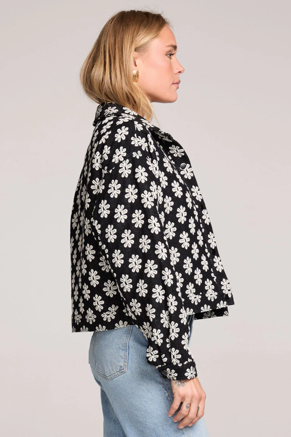 Woman wearing a black floral patterned jacket against a plain background