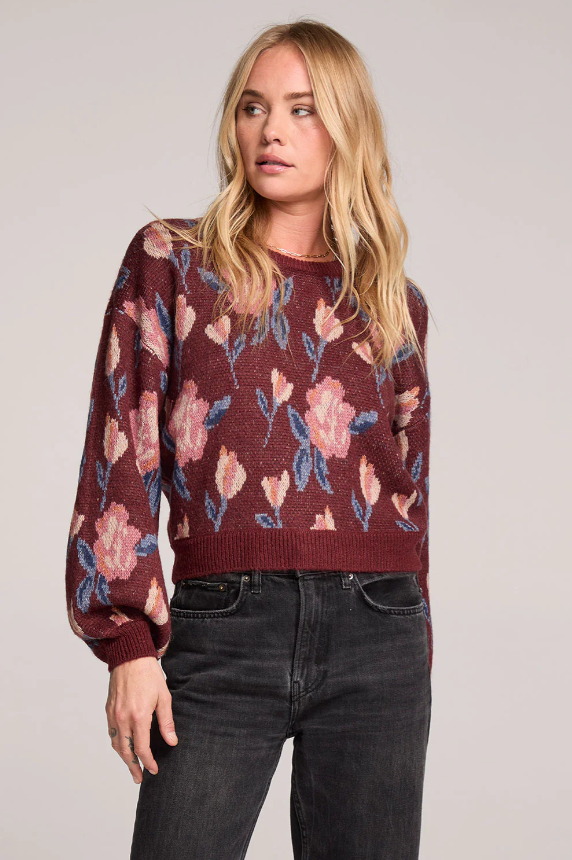 Woman wearing a red floral-patterned sweater and dark jeans against a plain background