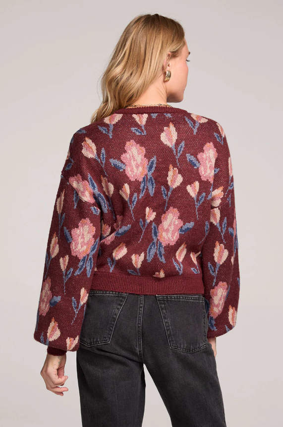 Person wearing a maroon sweater with floral pattern on a plain background