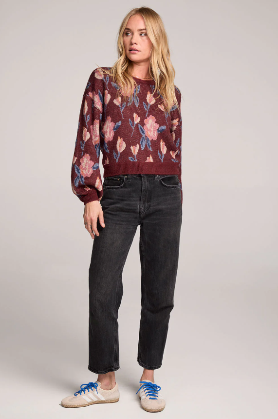 Woman wearing a floral patterned sweater and black jeans on a plain background