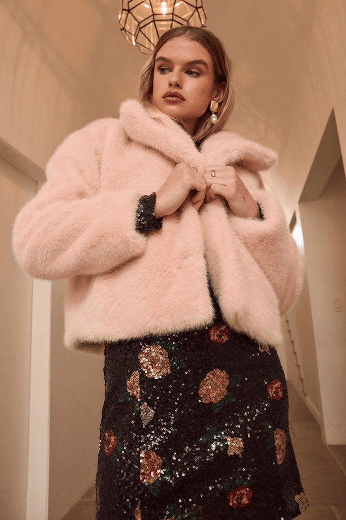 Woman wearing a pink fluffy coat and black floral dress in an indoor setting