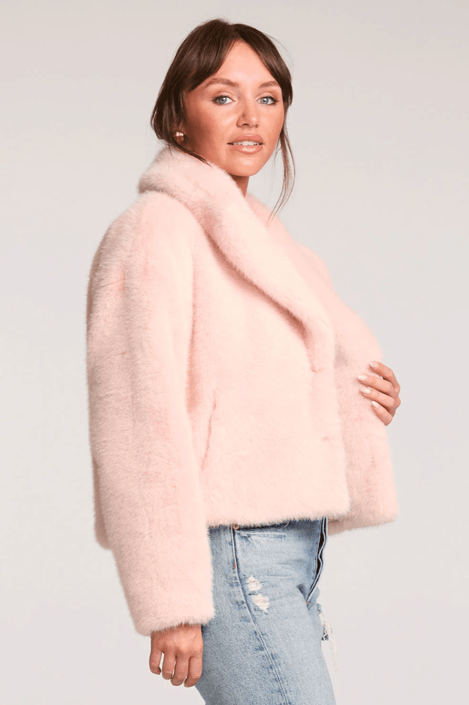 Woman wearing a light pink faux fur coat against a plain background