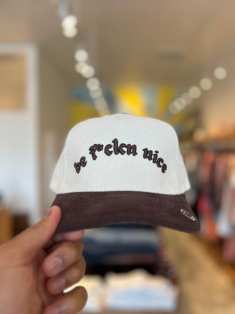 A white corduroy hat with a brown bill and embroidered text.