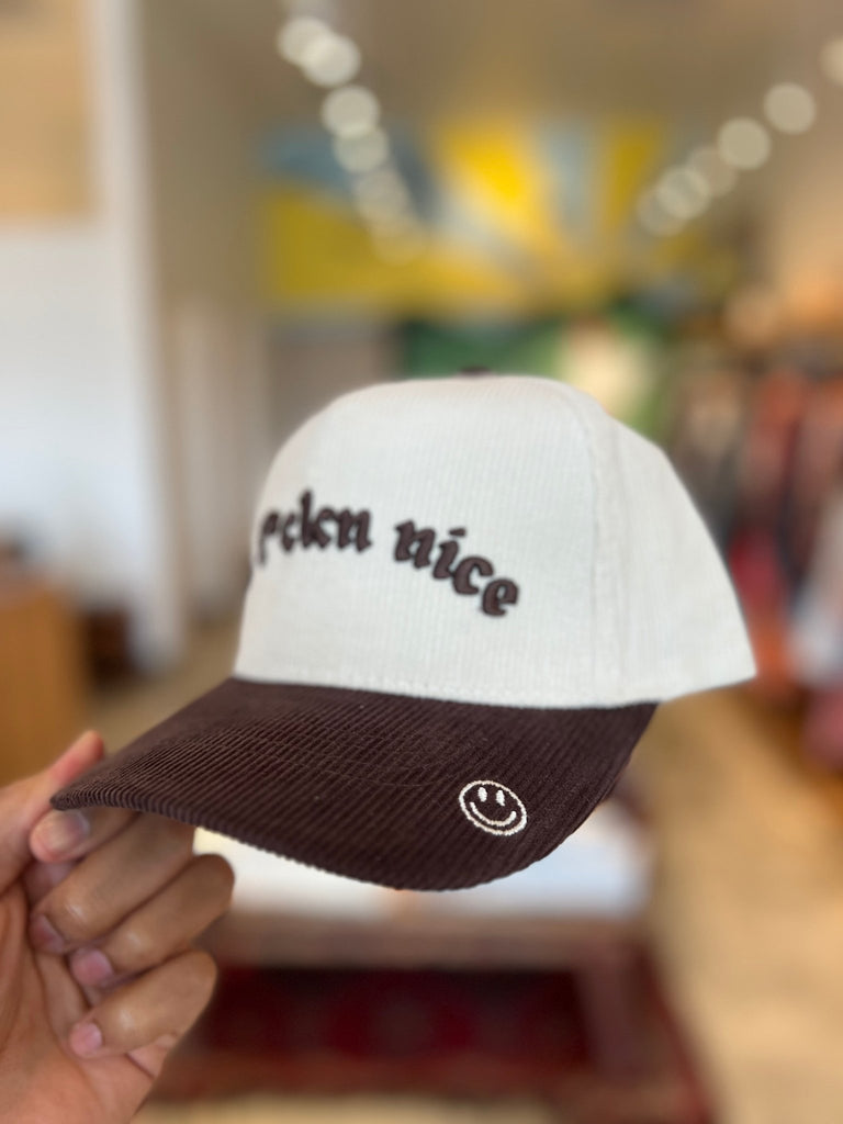 A white corduroy hat with a brown bill and embroidered text.