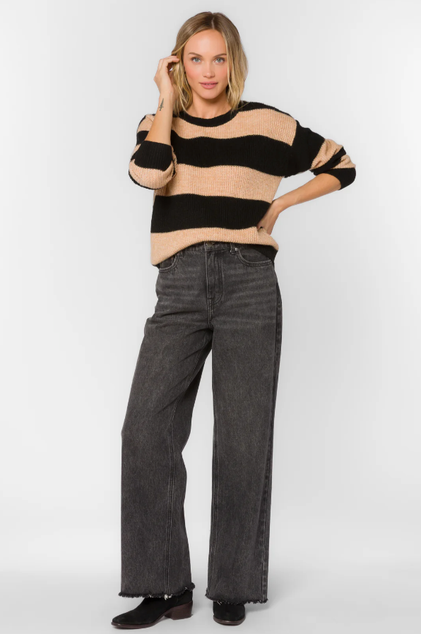 Woman wearing a black and beige striped sweater and dark jeans on a white background