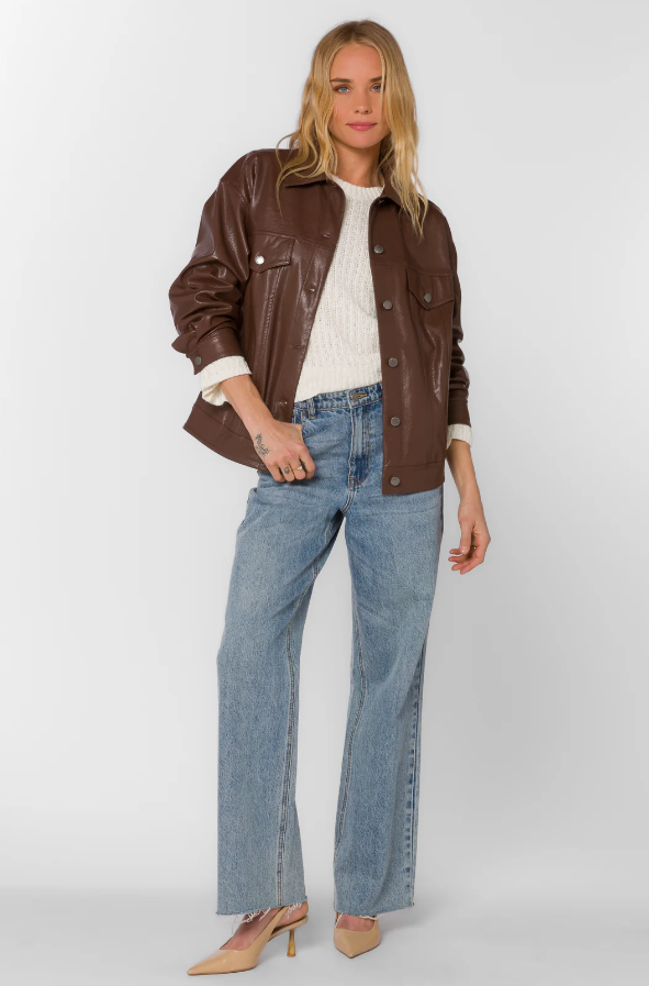Woman wearing a brown faux leather jacket, white shirt, and blue jeans on a white background